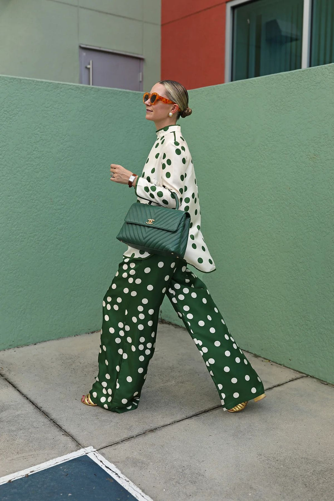 Woman in mismatched green polka dot matching set with Chanel bag on colorful street