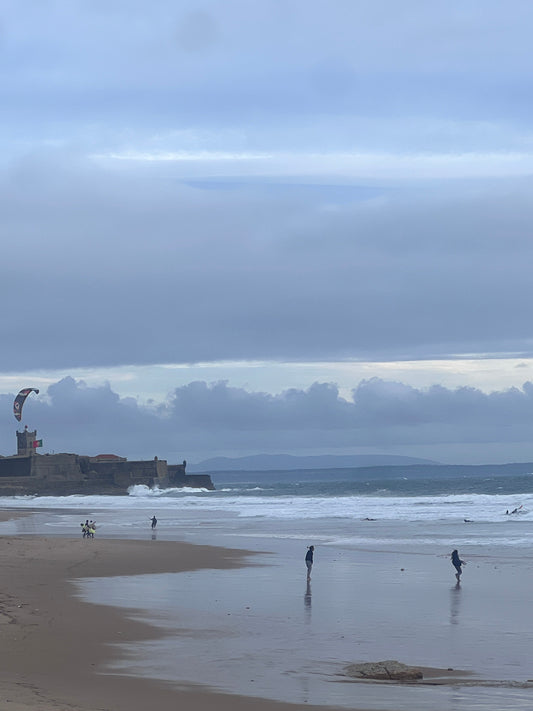 Stormy beach in Portugal with wet sand reflecting the sky and a kite surfer riding waves in the distance.